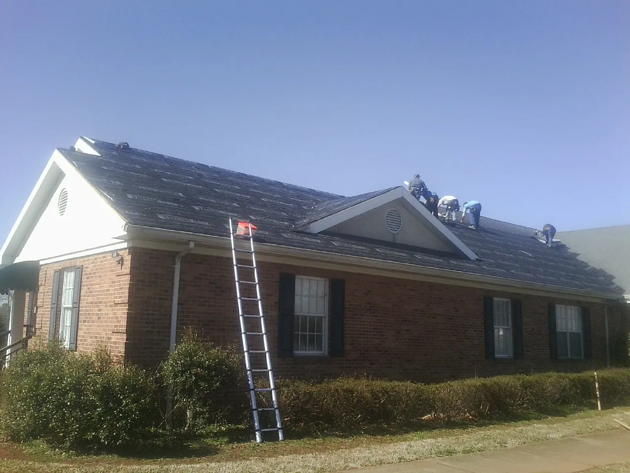 Crew tearing shingles off a brick ranch roof with a ladder set — Metal Roof Repair work by our crew in Kenneth