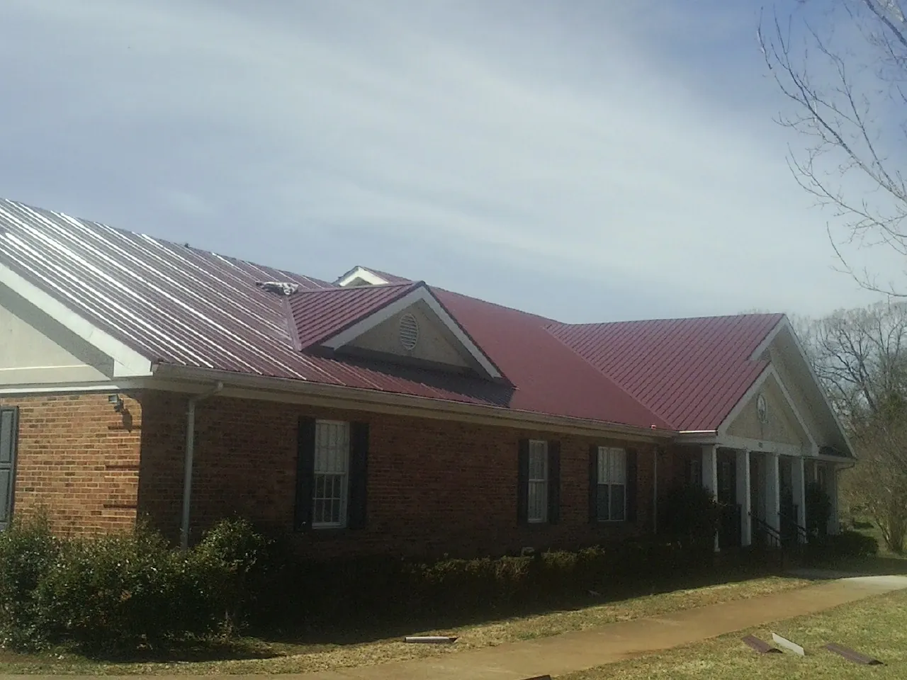 Red metal roof with gabled entries on a long brick building, from a Hail Damage Roof Repair job in Kenneth