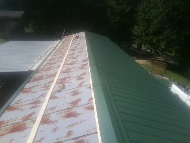 Old rusted panels beside newly installed green metal roofing — Wind Damage Roof Repair by Roofing Brothers in Kenneth