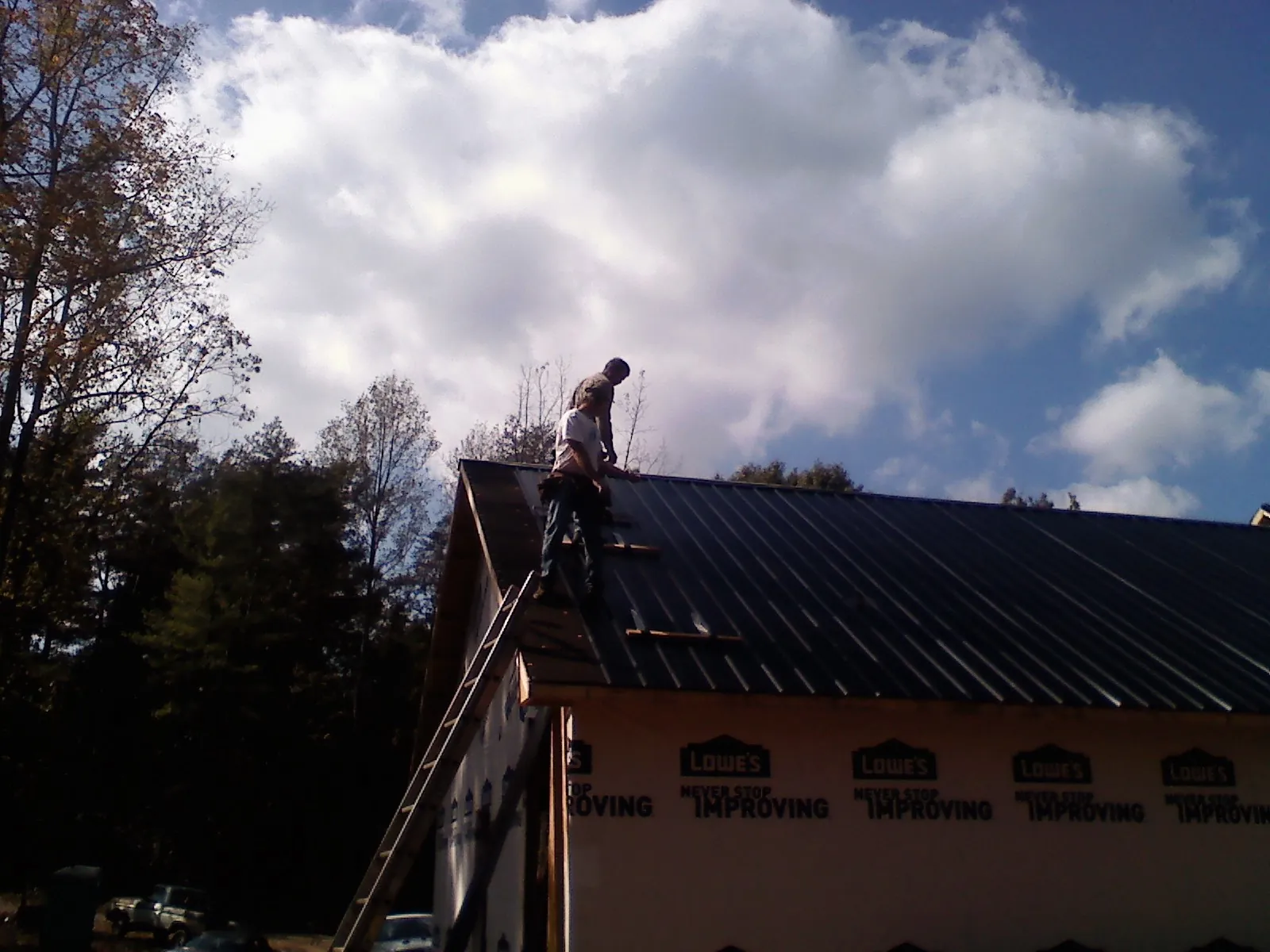 Roofer fastening dark metal panels high against a cloudy sky, from a Roof Inspection job in Kenneth
