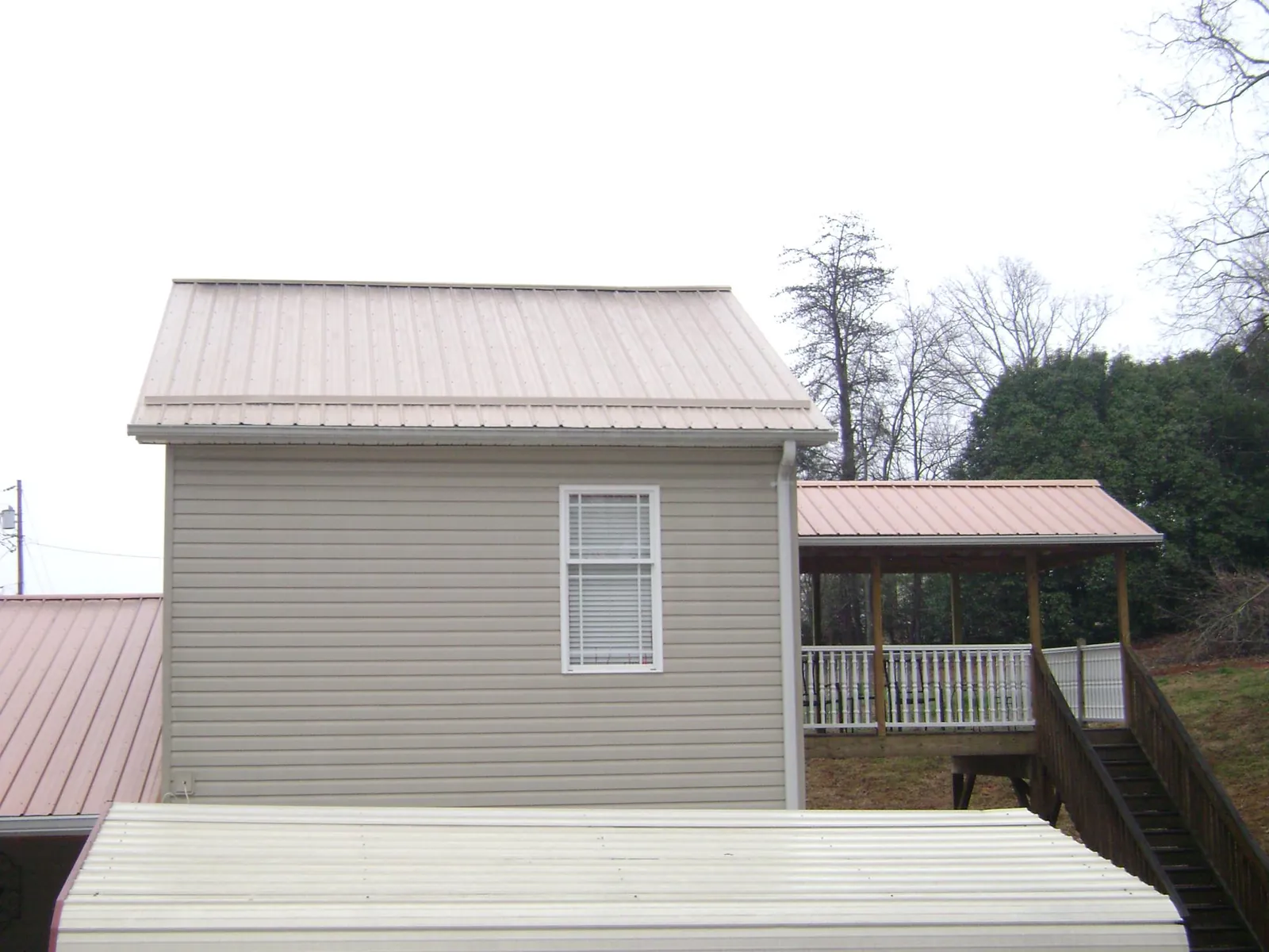 Tan metal roofs on a two story addition and attached porch, from a Roof Replacement job in Kenneth